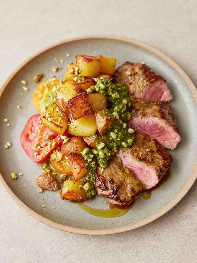 Plate with medium-rare steak, crispy potatoes and a chimichurri sauce drizzled on top