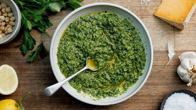 A bowl of vibrant green pesto surrounded by the ingredients to make it including nuts, herbs, Parmesan, garlic and lemon